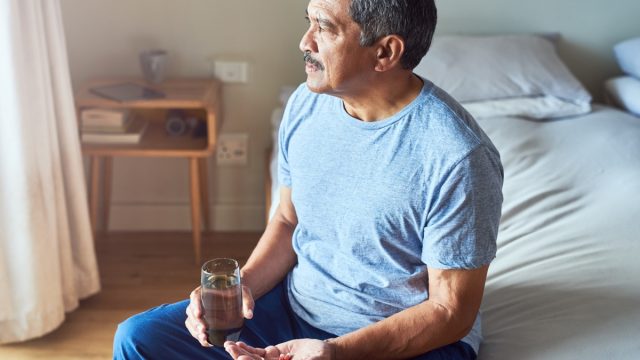 Shot of a cheerful mature man seated on his bed and about to drink medication with water in the bedroom at home during the day
