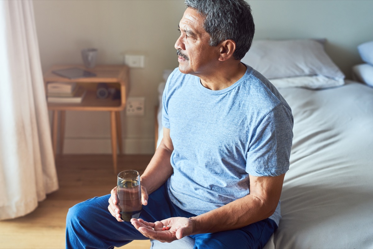 Shot of a cheerful mature man seated on his bed and about to drink medication with water in the bedroom at home during the day