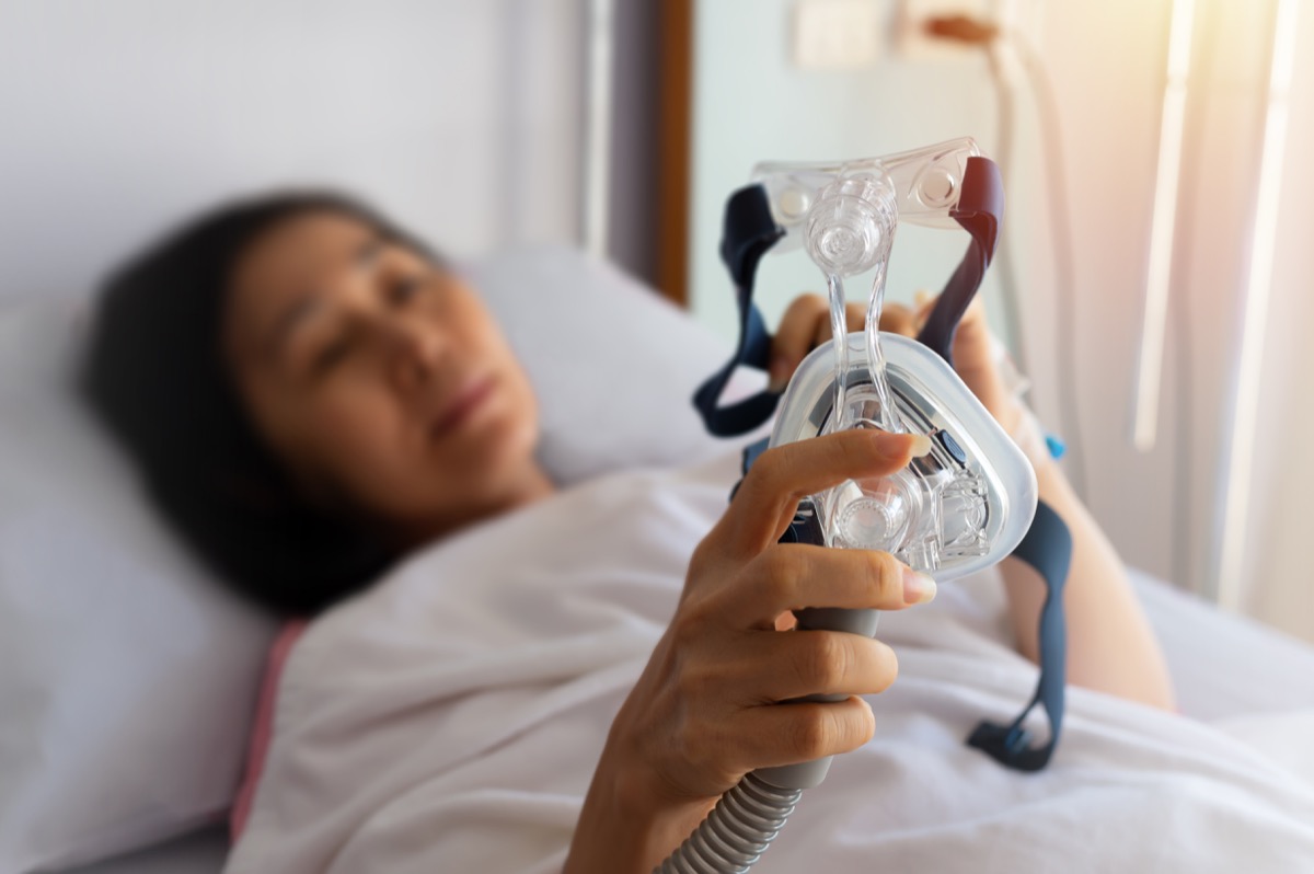 Elderly patient woman's hands holding CPAP mask lying in hospital room, selectively focused.  Obstructive sleep apnea therapy.