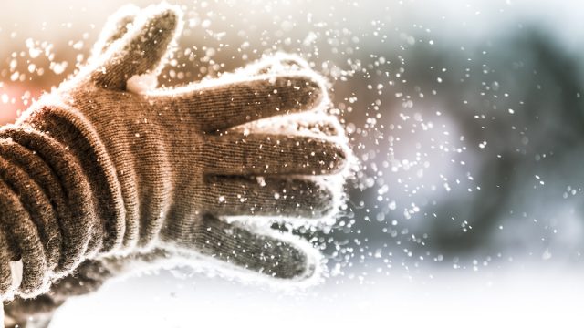 Closeup of person clapping winter gloves together as snow falls from them