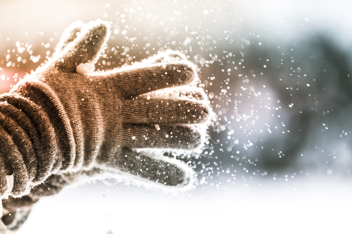 Cận cảnh một người vỗ tay vào găng tay mùa đông khi tuyết rơi từ chúng