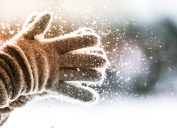 Closeup of person clapping winter gloves together as snow falls from them