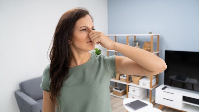 young woman in living room holding nose due to a bad smell