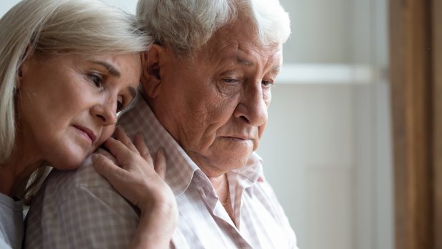 A middle-aged woman hugging an older man suffering from dementia
