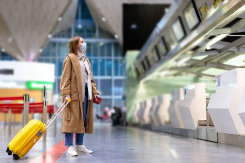 A woman wearing a face mask standing in an empty airport with her suitcase