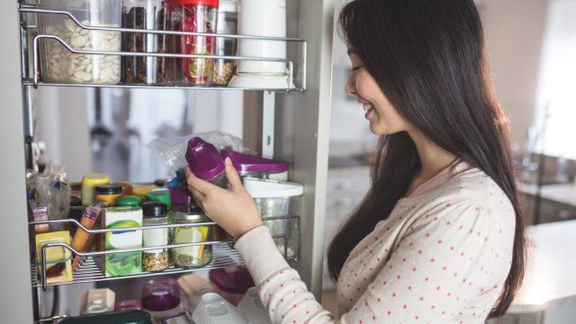 woman looking in cabinet and holding bottle with purple top