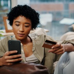 Young woman holding her credit card while using her cellphone at home