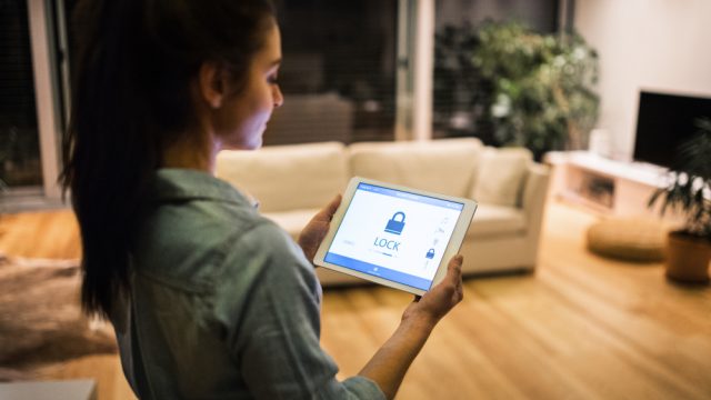 A woman standing in her living room using a tablet to control her home security system