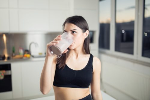 young woman in black leggings and sports bra drinking protein shake