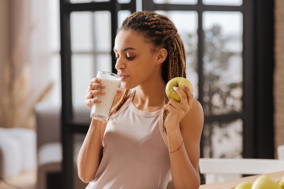 young woman drinking protein shake and holding green apple