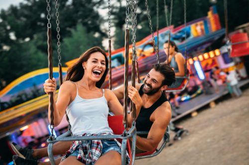 Man and woman riding swings at amusement park