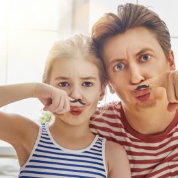 Father and young daughter with fake mustaches painted to their fingers