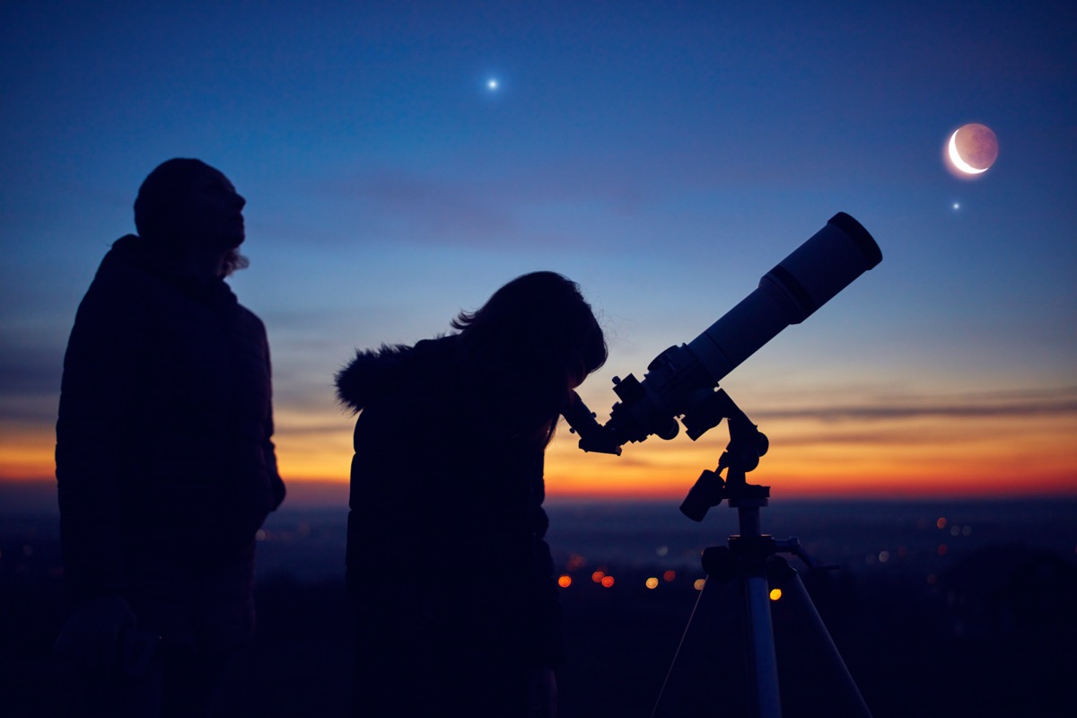 Two people looking at moon through telescope