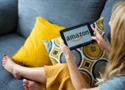 Poznan, Poland, 3.09.2019. Close up on woman's hands holding tablet with Amazon logo. Young woman using tablet with Amazon logo on the screen at cozy home on sofa in living room.