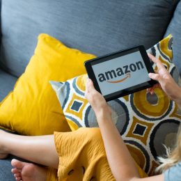 Poznan, Poland, 3.09.2019. Close up on woman's hands holding tablet with Amazon logo. Young woman using tablet with Amazon logo on the screen at cozy home on sofa in living room.