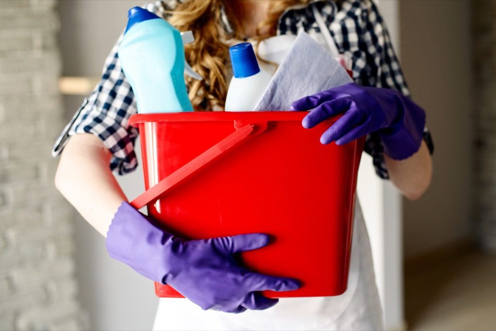 A close up of a person holding a bucket filled with cleaning supplies