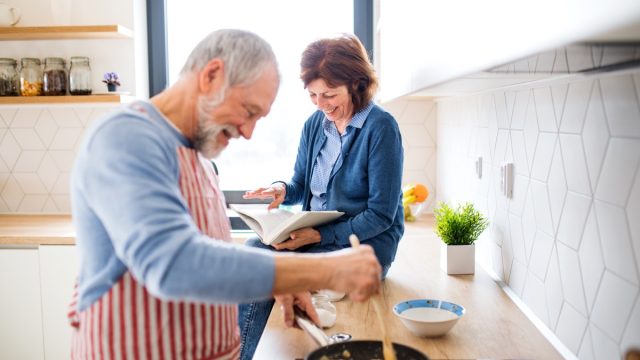 A portrait of happy senior couple in love indoors at home, cooking.