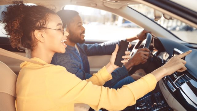 young couple driving car and woman is pointing to road ahead