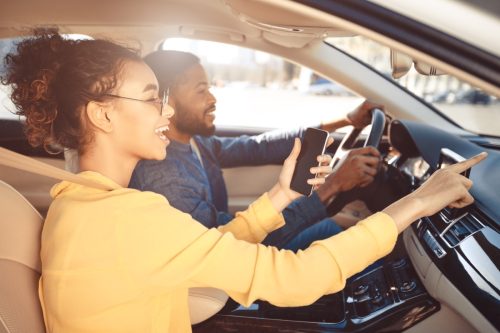 young couple driving car and woman is pointing to road ahead