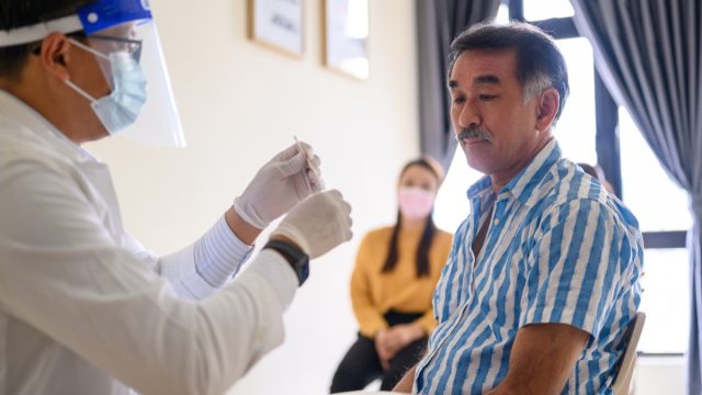 Doctor making a swab test to a mature man for corona virus (covid-19) pandemic disease. Covid-19 nasal swab test - doctor taking a mucus sample from patient nose in hospital.