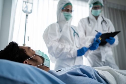 Ein Arzt im Schutzanzug diagnostiziert einen Covid-Patienten auf einem Krankenhausbett