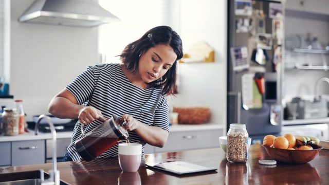Shot of an attractive young woman drinking coffee while using a digital tablet at home