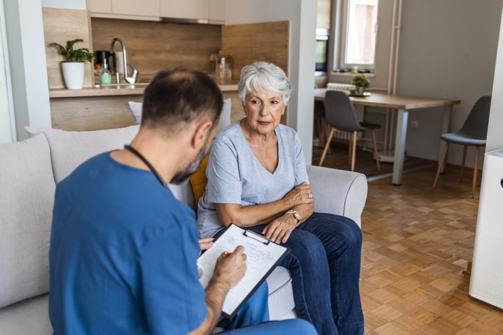 Happy mature doctor talking to senior female patient while being in a home visit.