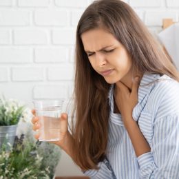 woman holding throat while drinking water