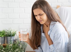 woman holding throat while drinking water