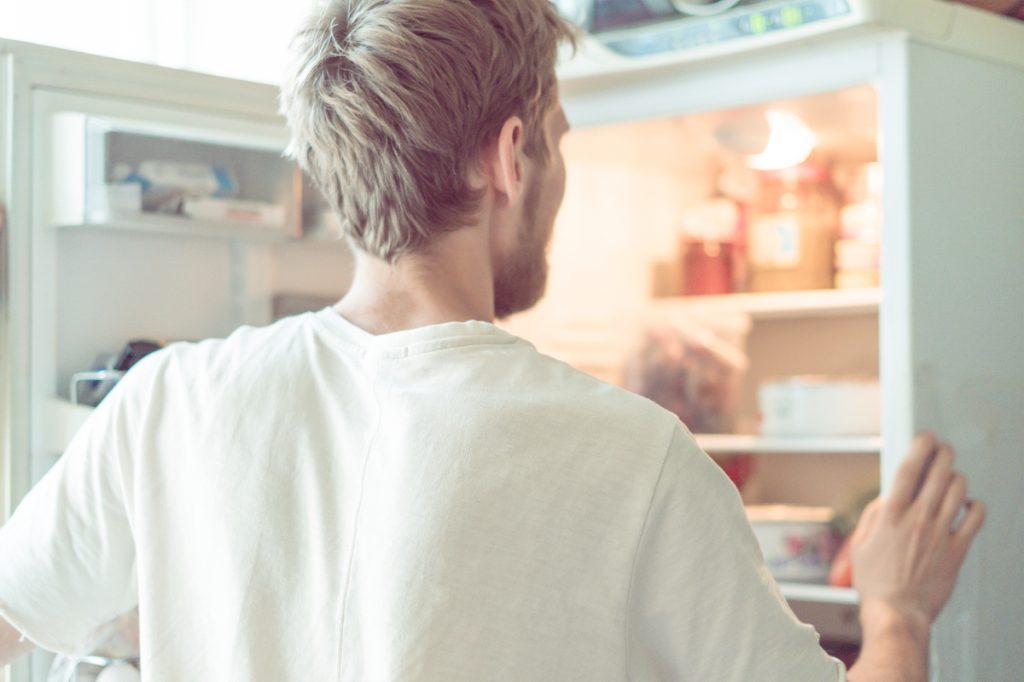 young man searching for food in fridge at home