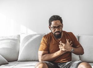 Man with high blood pressure experiencing chest pain while sitting at home during the day.