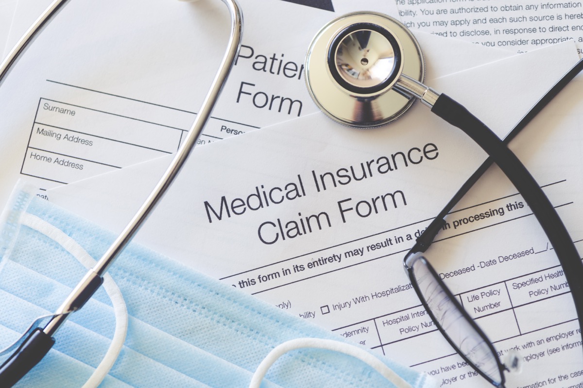 Medical Insurance claim form with stethoscope and surgical face mask. There are also other pieces of paperwork on the desk including a patient form