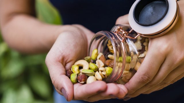 Brunette model hand holding glass hermetic pot with mix of nuts.