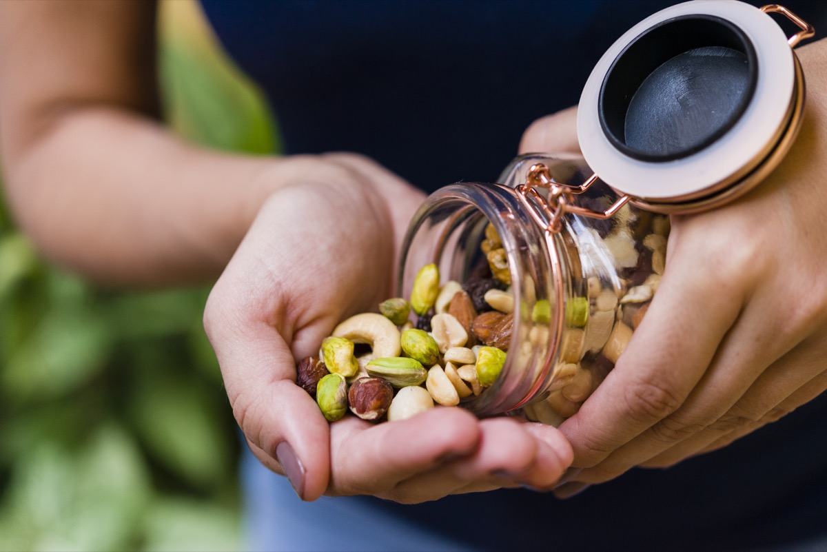 Brunette model hand holding glass airtight jar with mixed nuts.
