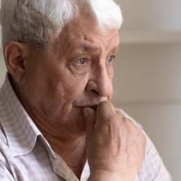 A senior man sitting with a concerned look on his face, potentially suffering from dementia
