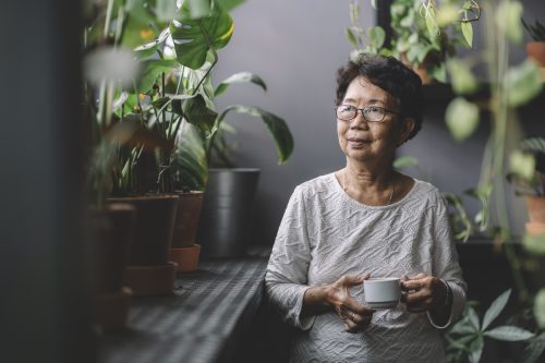 A senior woman drinking coffee while surrounded by houseplants