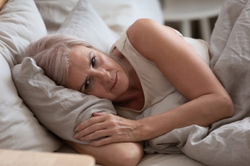 A senior woman lying awake in bed with a worried look on her face