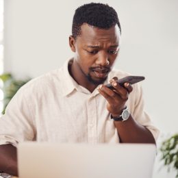 Shot of a young businessman talking on a cellphone while using a laptop in an office