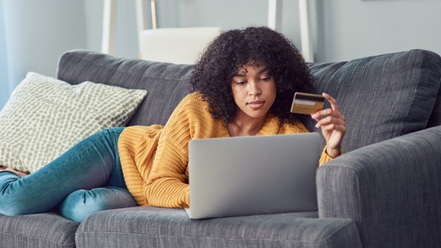 Shot of a young woman using a laptop and credit card on the sofa at home