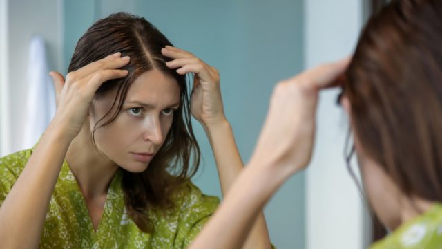 A young woman checking her hair in the mirror for gray strands