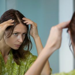 A young woman checking her hair in the mirror for gray strands