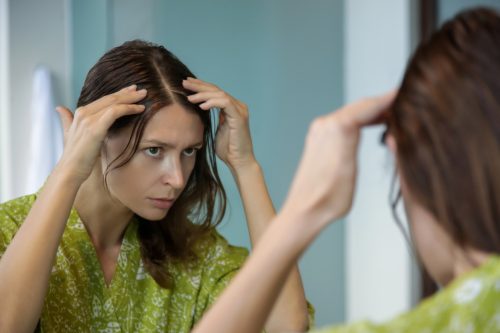 Uma jovem verificando o cabelo no espelho em busca de fios grisalhos