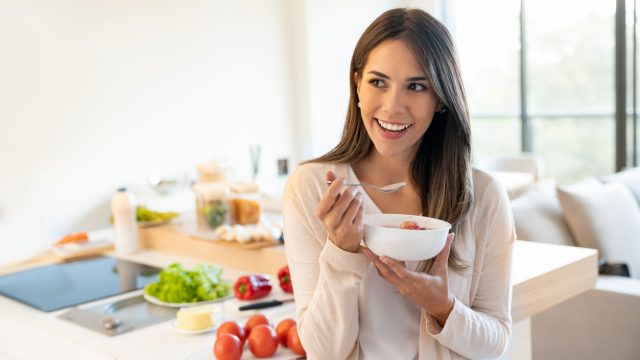 A young woman eating a bowl of yogurt in the kicthen