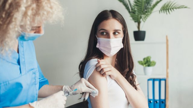 Young woman getting vaccinated by a nurse in a medical room.