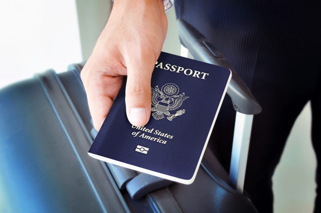 Close-up of someone holding an American passport over their suitcase