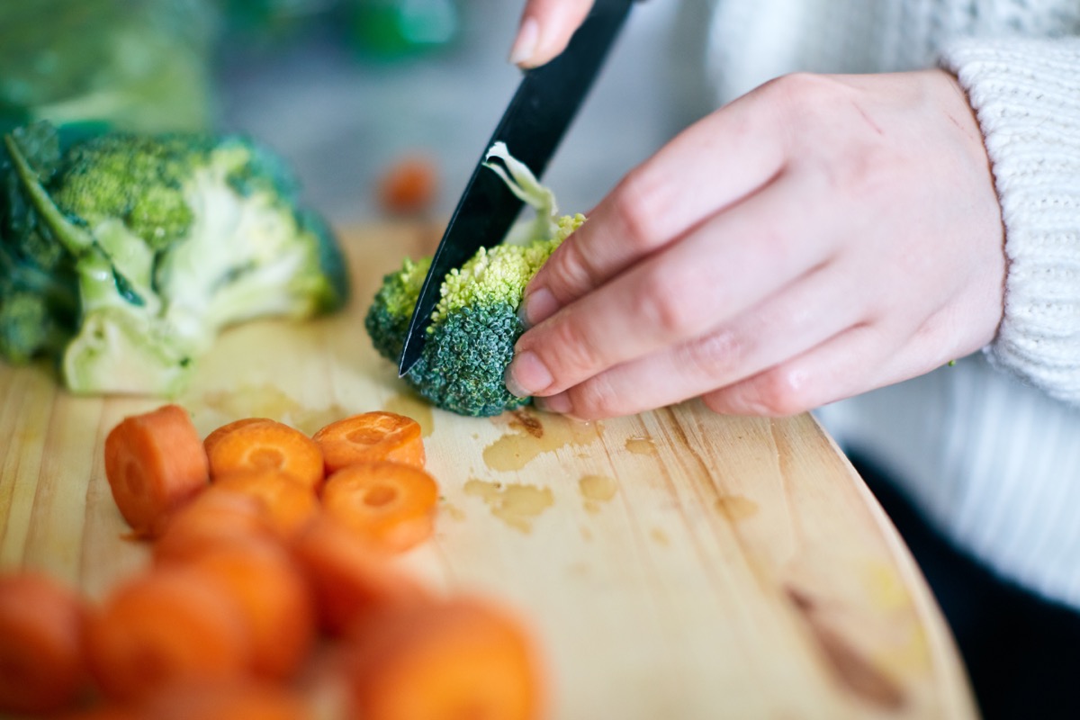 A woman carefully slices raw broccoli on a wooden board.