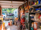 This photograph is of a garage lined with shelves full of things stored at home including, tools, cleaning supplies, holiday decorations and sporting equipment. The garage door is open.