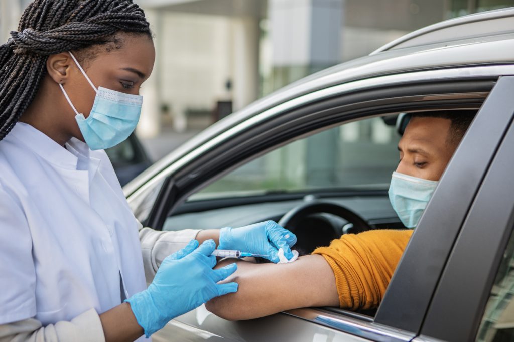 A healthcare professional giving a man COVID-19 vaccine while he sits in his car