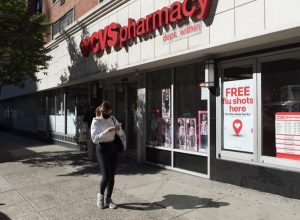Manhattan, New York. October 08, 2020. A woman wearing a face mask walks in front of a CVS pharmacy Midtown with a sigh advertising free flu shots.