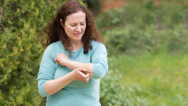 Woman scratching arm because it stings in a park with copy space